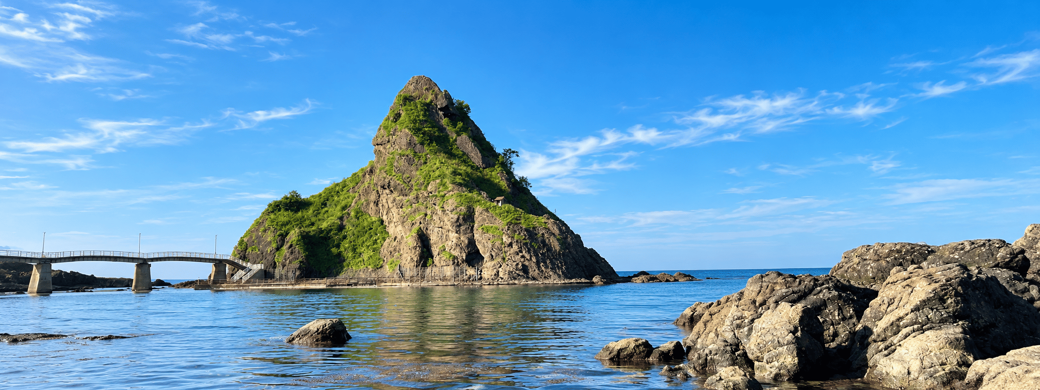 北海道の海岸、穏やかな青い海に浮かぶ緑の岩島